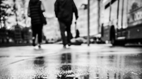 Fotografía en blanco y negro de unas personas alejándose con su silueta reflejada en un charco