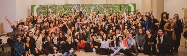 Imagen grupo grande de mujeres unas sentadas y otras de pie en un aula, saludando a la cámara